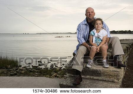 Stock Photograph - Portrait of a girl sitting by her father with a lake in the background. Fotosearch