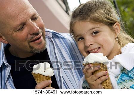 Stock Image - Portrait of a girl sitting with her father and eating ice cream. Fotosearch