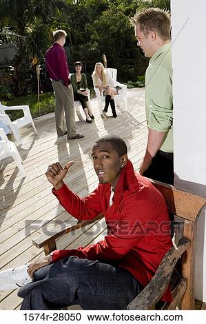 Portrait of a man sitting on armchair while pointing out at friends View Large Photo Image Stock Image - Portrait of a man sitting on armchair while pointing out at friends. Fotosearch