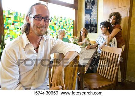 Portrait of a mature man smiling while others sitting by table View Large Photo Image Stock Photo - Portrait of a mature man smiling while others sitting by table. Fotosearch