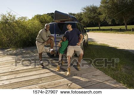 Portrait of a mature man standing with his son and friend by a car View Large Photo Image Stock Photo - Portrait of a mature man standing with his son and friend by a car. Fotosearch