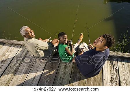 Stock Photo - Portrait of a mature man with his son and friend sitting on jetty. Fotosearch