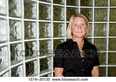 Stock Photography - Portrait of a mature woman standing in front of glass bricks. Fotosearch