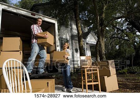 Stock Photo - Portrait of a mid adult couple unloading chairs and cardboard boxes from the moving van. Fotosearch