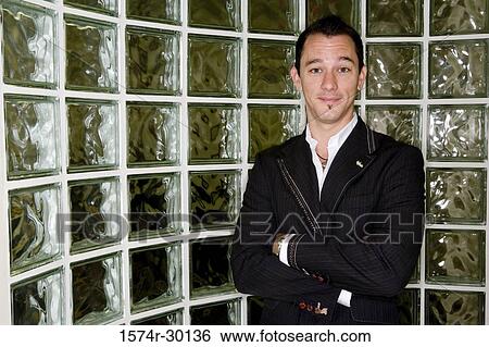 Stock Photograph - Portrait of a mid adult man standing in front of glass bricks. Fotosearch