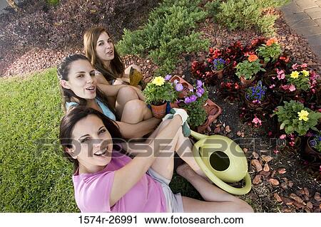 Stock Image - Portrait of a mother gardening with her daughters by watering pot in garden. Fotosearch