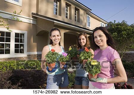 Stock Image - Portrait of a mother holding potted plant with her daughters in garden. Fotosearch