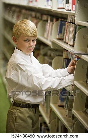 Stock Image - Portrait of a schoolboy standing by shelf in the library. Fotosearch