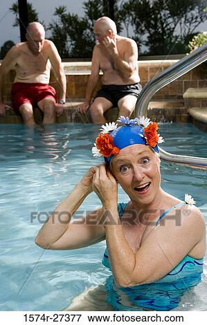 Stock Photo - Portrait of a senior woman in swimming pool while senior men discussing in the background. Fotosearch