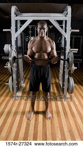 Picture - Portrait of a shirtless young man working out with barbells. Fotosearch