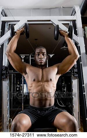 Stock Image - Portrait of a shirtless young man working out with dumbbells. Fotosearch