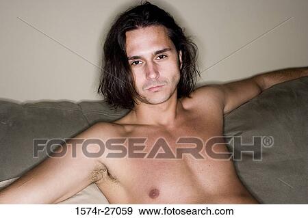 Stock Photo - Portrait of a shirtless young man sitting on sofa. Fotosearch