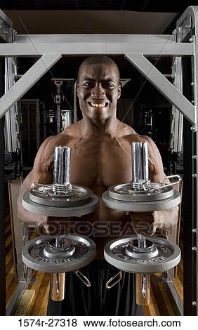 Stock Photo - Portrait of a shirtless young man working out with dumbbells. Fotosearch