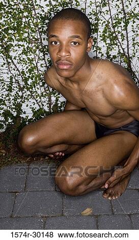 Portrait of a shirtless young man crouching View Large Photo Image Stock Photo - Portrait of a shirtless young man crouching. Fotosearch