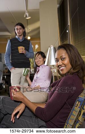 Portrait of a smiling businesswoman with colleagues holding tea cup in an office View Large Photo Image Picture - Portrait of a smiling businesswoman with colleagues holding tea cup in an office. Fotosearch