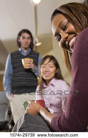 Portrait of a smiling businesswoman with colleagues holding tea cup in an office View Large Photo Image Stock Photo - Portrait of a smiling businesswoman with colleagues holding tea cup in an office. Fotosearch