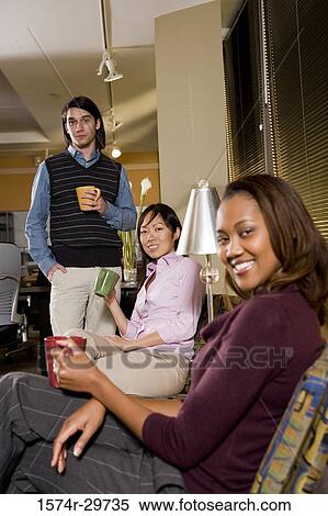 Portrait of a smiling businesswoman with colleagues holding tea cup in an office View Large Photo Image Stock Photography - Portrait of a smiling businesswoman with colleagues holding tea cup in an office. Fotosearch