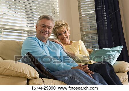 Stock Image - Portrait of a smiling mature couple sitting on a couch in living room. Fotosearch