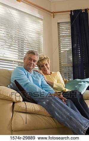 Portrait of a smiling mature couple sitting on a couch in living room View Large Photo Image Stock Photo - Portrait of a smiling mature couple sitting on a couch in living room. Fotosearch