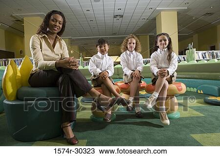 Portrait of a smiling teacher and schoolgirls sitting on stools in the library View Large Photo Image Stock Image - Portrait of a smiling teacher and schoolgirls sitting on stools in the library. Fotosearch