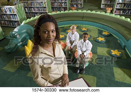Portrait of a smiling teacher holding book while schoolboys sitting on stools in the library View Large Photo Image Stock Image - Portrait of a smiling teacher holding book while schoolboys sitting on stools in the library. Fotosearch
