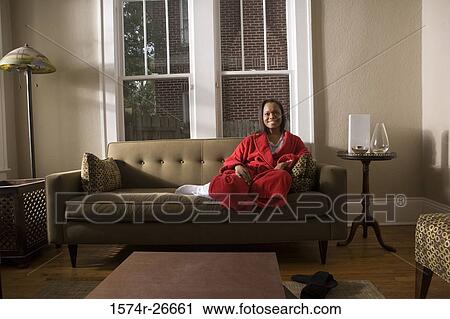 Stock Image - Portrait of a smiling young woman in gown sitting on a sofa. Fotosearch