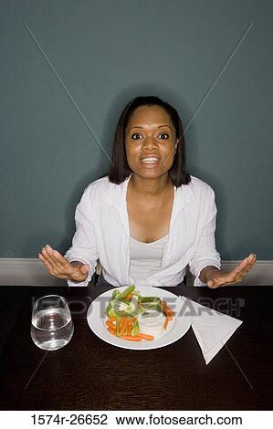 Portrait of a smiling young woman sitting by table with a plate of vegetables View Large Photo Image Stock Image - Portrait of a smiling young woman sitting by table with a plate of vegetables. Fotosearch