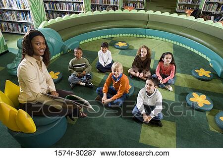 Portrait of a teacher holding book with students sitting on floor in the library View Large Photo Image Stock Photo - Portrait of a teacher holding book with students sitting on floor in the library. Fotosearch