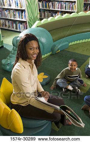 Portrait of a teacher holding book with students sitting on floor in the library View Large Photo Image Stock Photo - Portrait of a teacher holding book with students sitting on floor in the library. Fotosearch