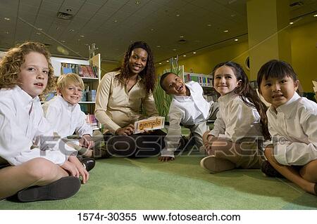 Stock Photography - Portrait of a teacher holding flash cards and sitting with students on floor in the library. Fotosearch