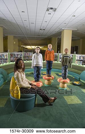 Stock Photo - Portrait of a teacher sitting while schoolboys standing on stools in the library. Fotosearch