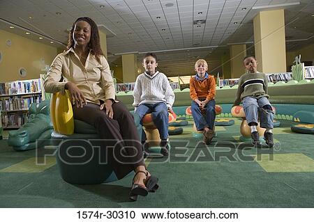 Stock Image - Portrait of a teacher sitting with schoolboys in the library. Fotosearch