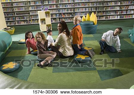 Portrait of a teacher sitting with students looking over shoulder in the library View Large Photo Image Stock Photograph - Portrait of a teacher sitting with students looking over shoulder in the library. Fotosearch