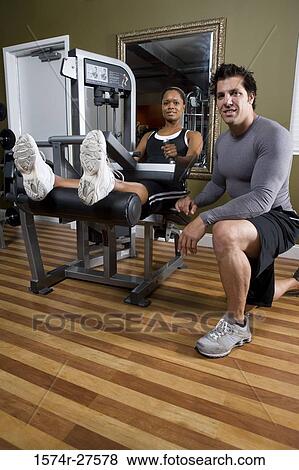 Stock Photo - Portrait of a trainer crouching by a young woman in the gym. Fotosearch