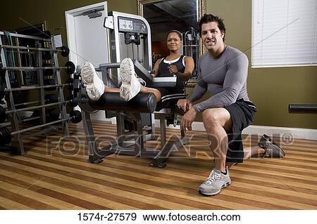 Portrait of a trainer crouching by a young woman in the gym View Large Photo Image Stock Photo - Portrait of a trainer crouching by a young woman in the gym. Fotosearch