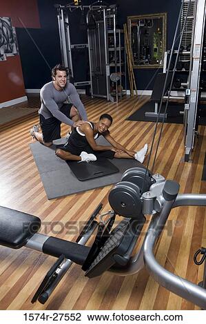 Stock Image - Portrait of a trainer helping out of a young woman in the gym. Fotosearch