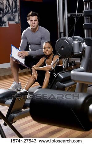 Portrait of a trainer holding a file by a young woman in the gym View Large Photo Image Stock Image - Portrait of a trainer holding a file by a young woman in the gym. Fotosearch