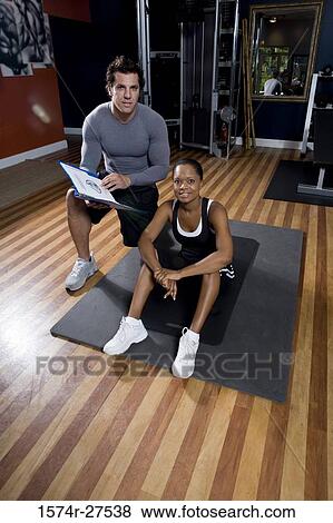 Portrait of a trainer holding a file by a young woman in the gym View Large Photo Image Stock Photo - Portrait of a trainer holding a file by a young woman in the gym. Fotosearch