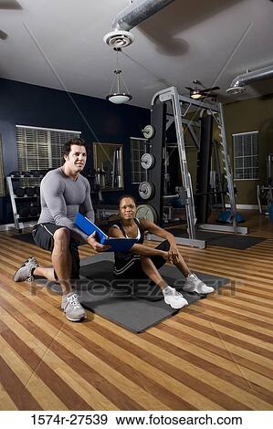 Portrait of a trainer holding a file by a young woman in the gym View Large Photo Image Stock Photo - Portrait of a trainer holding a file by a young woman in the gym. Fotosearch