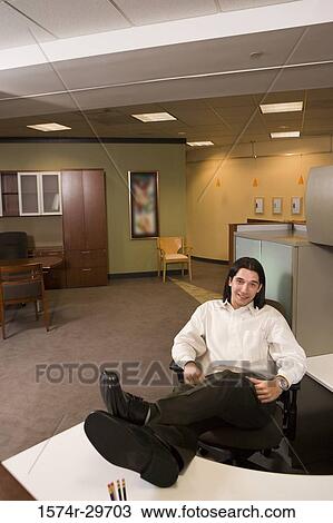 Portrait of a young businessman sitting in an office with his legs on desk View Large Photo Image Stock Image - Portrait of a young businessman sitting in an office with his legs on desk. Fotosearch