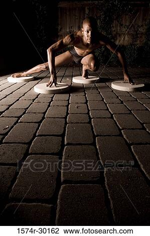 Stock Image - Portrait of a young man crouching on the round tiles. Fotosearch