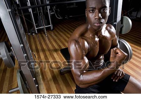 Stock Image - Portrait of a young man flexing muscles in the gym. Fotosearch