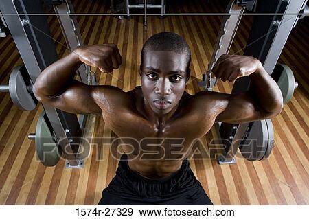 Stock Photo - Portrait of a young man flexing muscles in the gym. Fotosearch