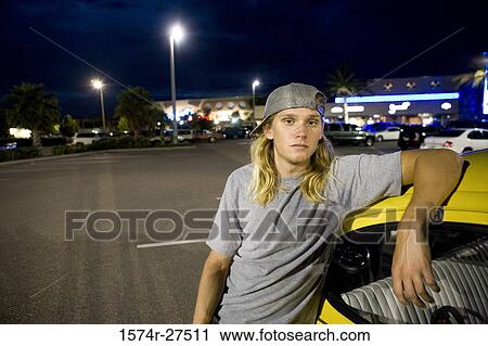 Stock Image - Portrait of a young man leaning by a car at the parking area. Fotosearch