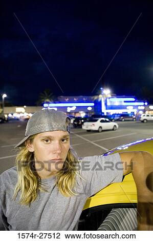 Stock Image - Portrait of a young man leaning by a car at the parking area. Fotosearch