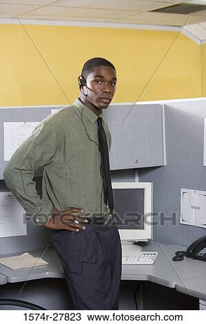 Portrait of a young man standing by a computer in an office View Large Photo Image Stock Image - Portrait of a young man standing by a computer in an office. Fotosearch