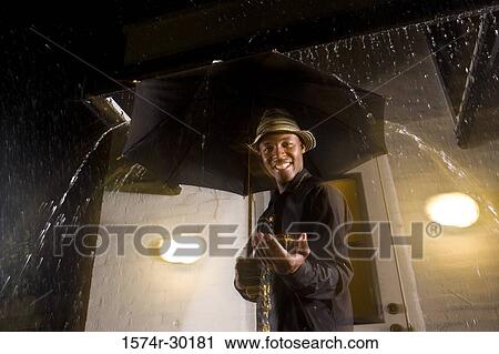 Portrait of a young man standing in front of the door under an umbrella View Large Photo Image Stock Image - Portrait of a young man standing in front of the door under an umbrella. Fotosearch