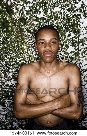Stock Image - Portrait of a young man standing with arms crossed. Fotosearch