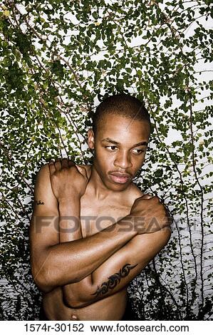 Stock Image - Portrait of a young man standing with arms crossed. Fotosearch