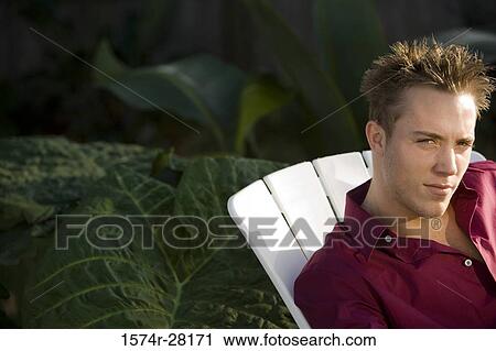 Stock Image - Portrait of a young man staring while sitting on armchair. Fotosearch